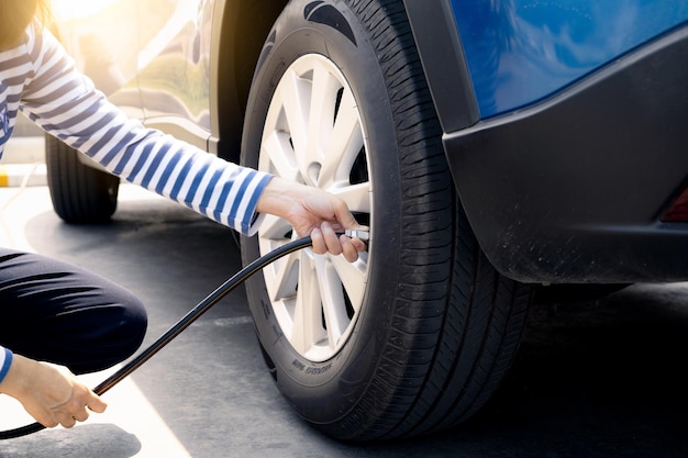 Femme gonfle le pneu Femme vérifiant la pression des pneus et pompant de l'air dans le pneu de la roue de la voiture Voiture