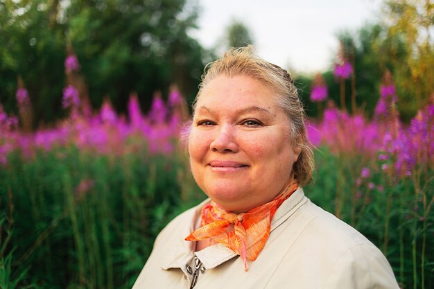 Femme de grande taille en sweat à capuche fuchsia regardant la caméra tout en se tenant au milieu de fleurs lumineuses dans un pré en campagne