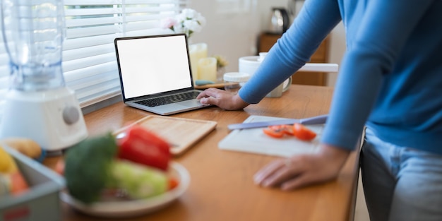 Une femme grasse joyeuse cuisinant dans la cuisine montrant un ordinateur portable sur un écran blanc vide à la maison.