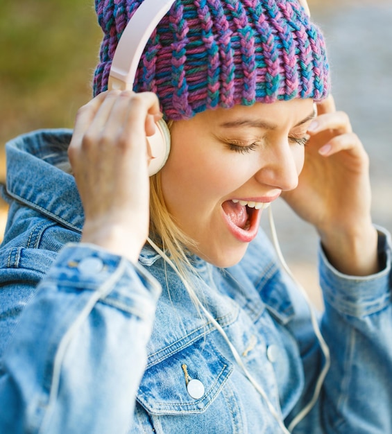 Femme avec gros casque Fille écoute de la musique dans les écouteurs Fille souriante musique relaxante un smartphone et un casque Portrait extérieur d'une fille à la mode Concept de mélodie d'automne Ambiance chaleureuse d'automne