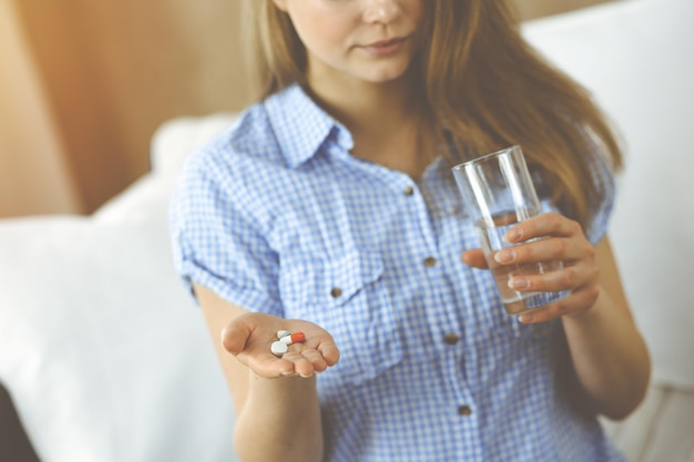 Femme en gros plan tenant des pilules le temps de prendre des médicaments, guérir les maux de tête. Concept de médecine pendant l'auto-isolement et la pandémie de coronavirus.