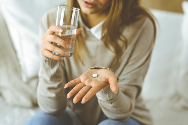 Femme en gros plan tenant des pilules le temps de prendre des médicaments, de guérir les maux de tête, l'hypertension artérielle ou le taux de cholestérol pour remédier aux analgésiques. Concept de séjour à la maison pendant la pandémie de coronavirus et moi-même