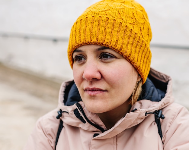 Femme de gros plan avec visage triste et vêtements d'hiver à côté du mur blanc