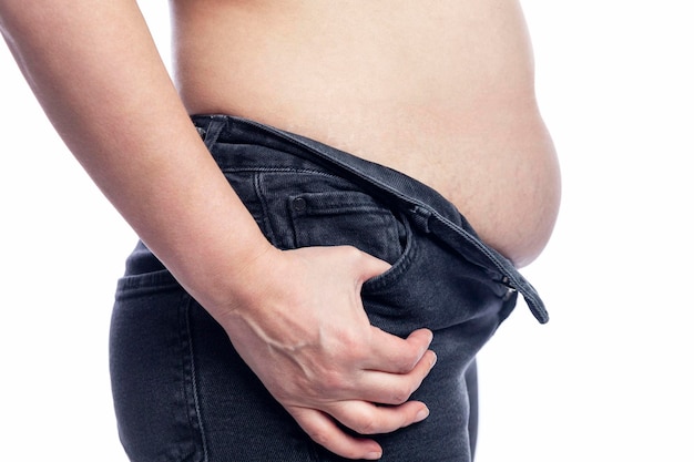 Une femme avec un gros ventre en jeans avec une braguette déboutonnée touche la graisse Joli corps en surpoids Gros plan Isolé sur fond blanc Vue latérale