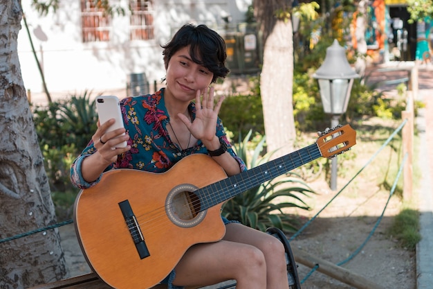 Femme avec guitare faisant un appel vidéo alors qu'il était assis dans un parc