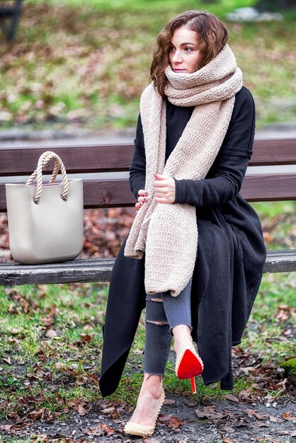 Femme habillée à la mode grande écharpe assise seule sur un banc dans le parc