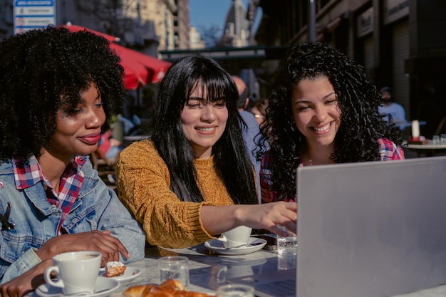 Femme haïtienne et femmes d'affaires latines ensemble dans un café en plein air analysant sur un ordinateur portable avec accès à Internet