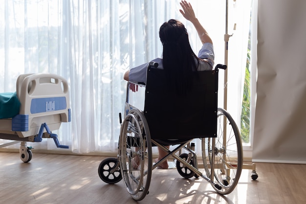 Une femme handicapée dans un fauteuil roulant est assise de la fenêtre dans la chambre du patient.