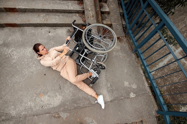 Une femme handicapée est allongée sur le sol près des escaliers près du fauteuil roulant. Le concept d'un fauteuil roulant, d'une personne handicapée, d'une vie pleine, d'une personne paralysée, handicapée.