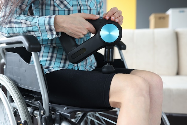 Femme handicapée en fauteuil roulant faisant un massage des jambes avec un masseur à percussion en gros plan