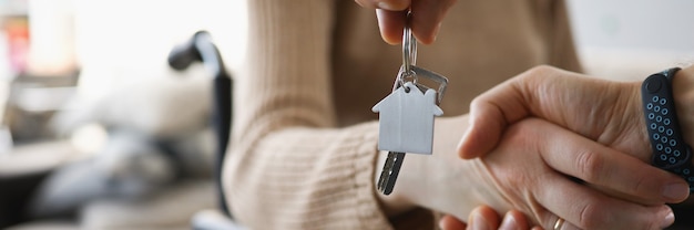 Femme handicapée en fauteuil roulant serrant la main d'un homme avec les clés du nouvel appartement en gros plan