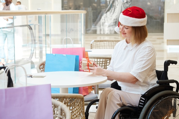 Une femme handicapée portant un bonnet de Noel avec des sacs à provisions