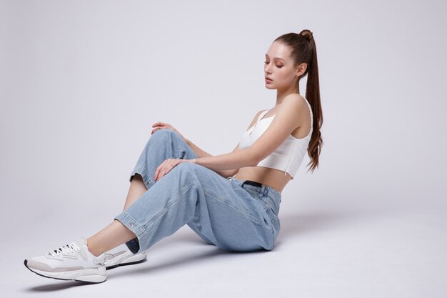 Femme en haut blanc baskets jeans bleu sur fond blanc Studio Shot Model est assis