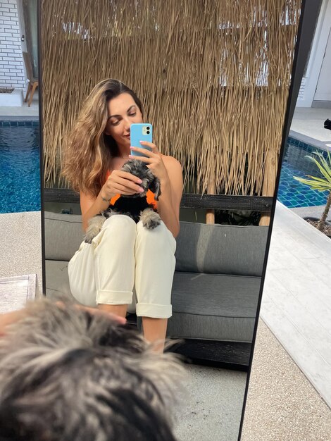 Femme en haut orange et pantalon confortable confortable à la maison en plein air prendre un selfie photo au téléphone avec un chiot minia