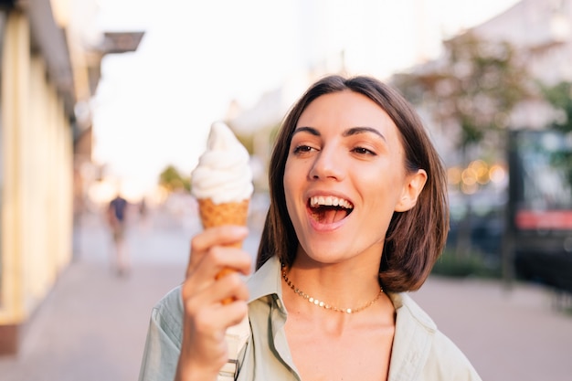 Femme à l'heure du coucher du soleil d'été ayant un cornet de crème glacée dans la rue de la ville
