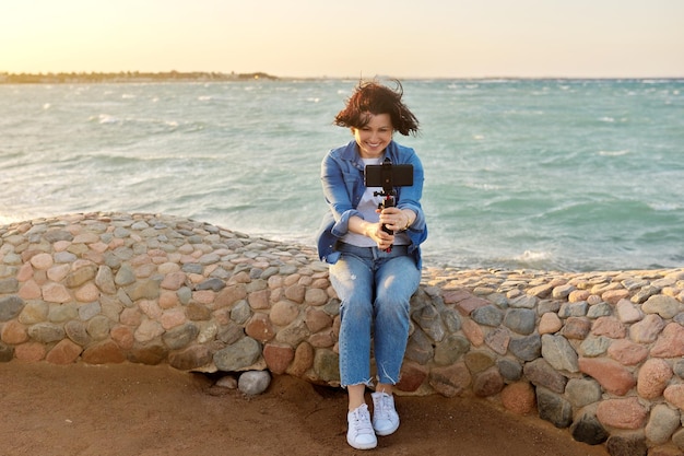 Femme heureuse d'âge moyen parlant d'enregistrement vidéo en ligne sur smartphone