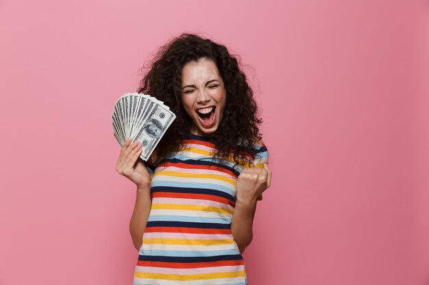 femme heureuse des années 20 aux cheveux bouclés tenant un ventilateur d'argent dollar isolé sur rose