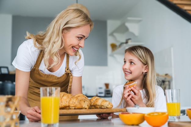 Une femme heureuse apporte à sa fille un croissant et un muffin cuits au four pour le petit-déjeuner