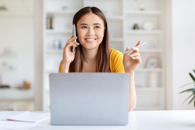 Une femme heureuse au téléphone avec un ordinateur portable au bureau.