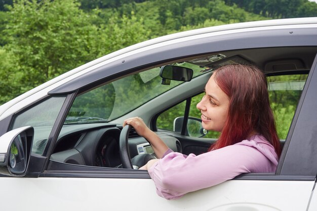 Une femme heureuse au volant d'une voiture regarde par la fenêtre la route.