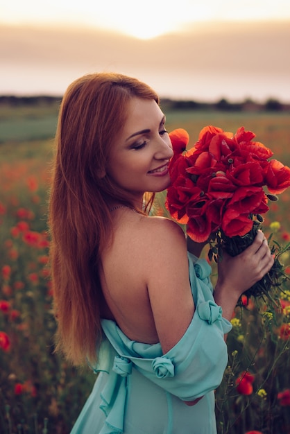 Femme heureuse aux yeux fermés tenant le bouquet de coquelicots au coucher du soleil, gros plan