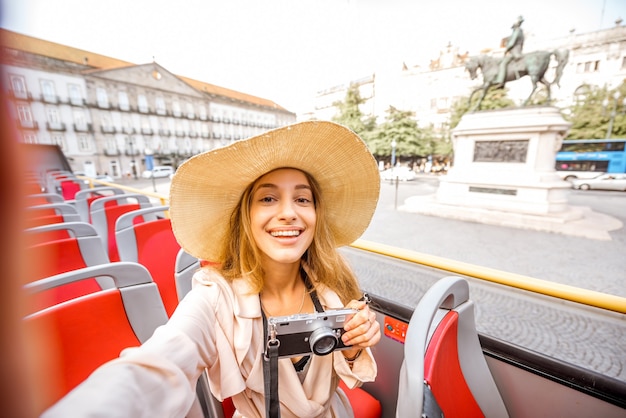 Femme heureuse ayant une excursion sur le bus touristique ouvert debout sur la place de la liberté dans la ville de Porto, Portugal