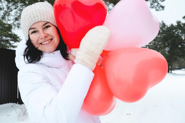 Femme heureuse avec des ballons en forme de coeur en plein air en hiver avec de la neige. Saint Valentin, amour et engouement, cadeau d'un petit ami, déclaration d'amour, style de vie