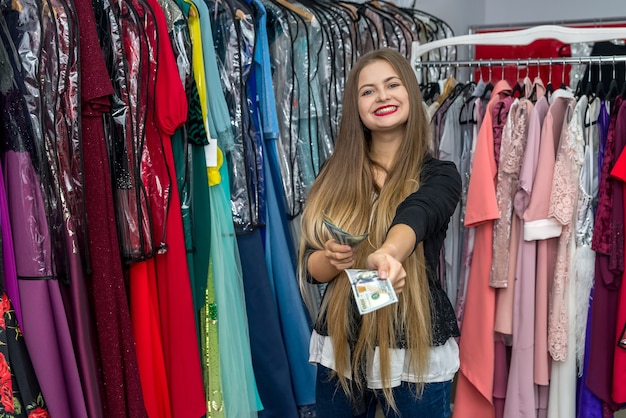 Femme heureuse avec des billets en dollars en magasin de vêtements