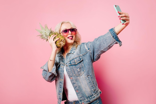 Femme heureuse blonde avec ananas posant sur un fond de couleur