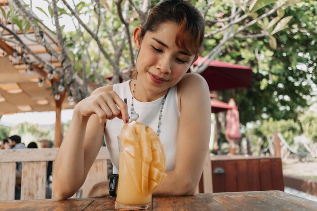 Une femme heureuse boit un smoothie au jus de mangue en journée d'été