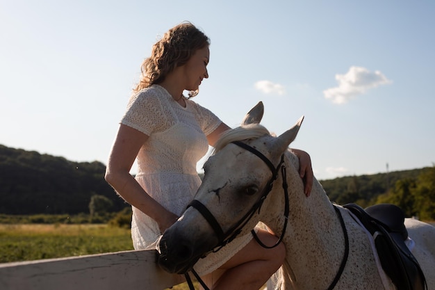 La femme heureuse caresse un cheval assis sur une clôture