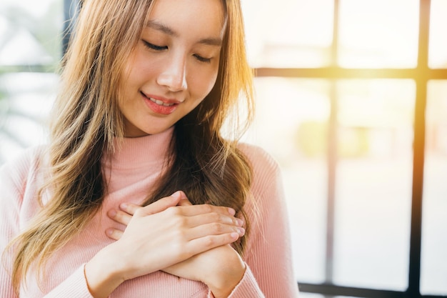 Photo une femme heureuse, charmante, souriante, tenant les mains, la poitrine près du cœur, honnête.