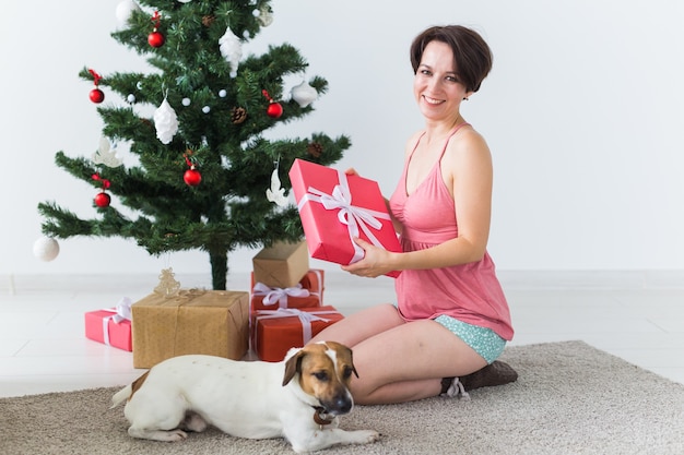 Femme heureuse avec chien ouvrant des cadeaux de Noël. Sapin de Noël avec des cadeaux en dessous. Décoré