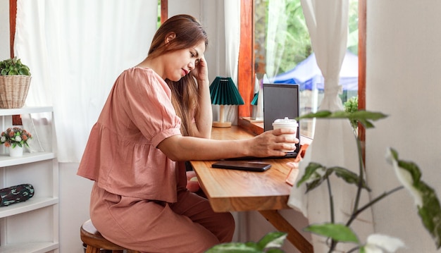 Une femme heureuse dans un café utilisant un ordinateur portable à la main et une tasse de café en papier