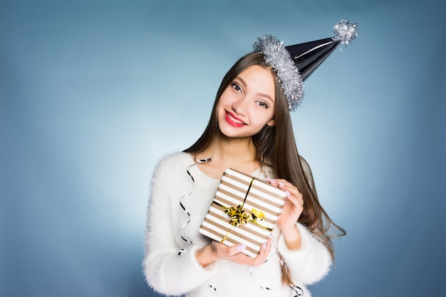 Une femme heureuse dans un chapeau de fête tient un cadeau dans ses mains