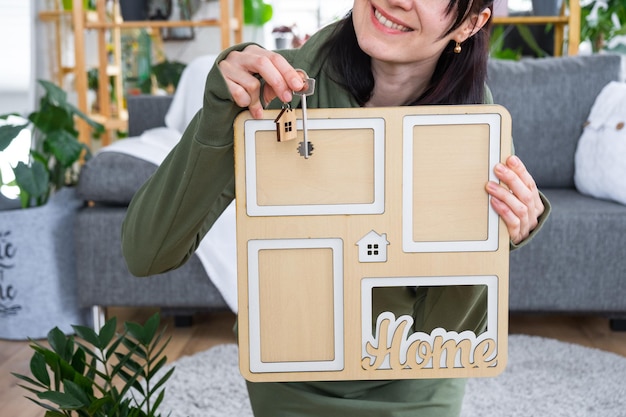 Photo femme heureuse dans la maison tient dans les mains cadre photo avec figure à la maison modèle et clé à l'intérieur projet de maison de rêve achat immobilier assurance hypothèque réservation de loyer