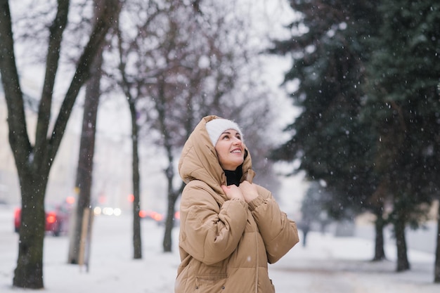 Une femme heureuse dans un manteau à capuchon Il se tient dans la ville en hiver sous la neige