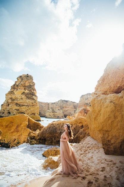 femme heureuse avec le dos dans une robe jaune debout sur la plage et la mer au coucher du soleil