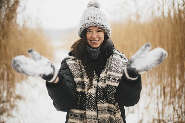 Femme heureuse élégante jetant de la neige dans des gants tricotés dans un parc enneigé Bonheur de l'heure d'hiver