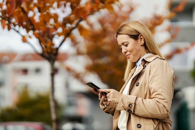 Une femme heureuse envoie des SMS dans la rue de la ville à l'automne