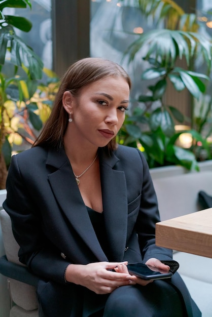 Une femme heureuse est assise dans un café de rue avec un smartphone à la main