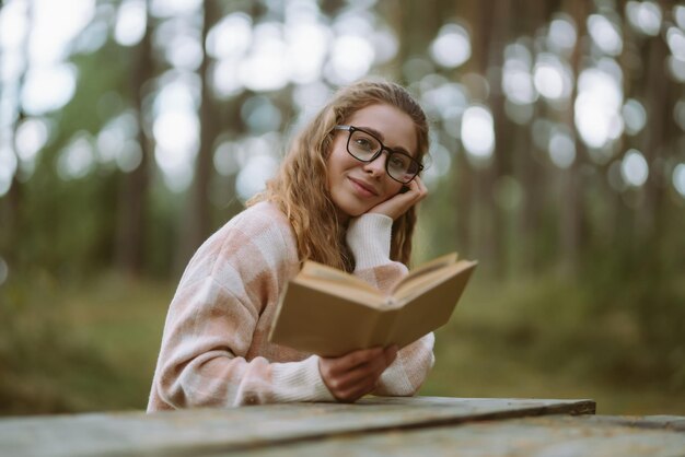Une femme heureuse est assise à table avec un livre dans une belle forêt Concept de style de vie de relaxation