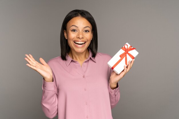 Une femme heureuse et excitée tient un cadeau dans une boîte emballée décorée se présente pour l'anniversaire de Noël ou du nouvel an