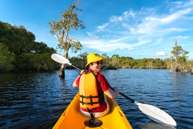 Femme heureuse faisant du kayak avec un bateau de kayak dans le lac nuture derrière la mer et la plage avant l'heure du coucher du soleil pour se détendre et pratiquer des sports nautiques extrêmes