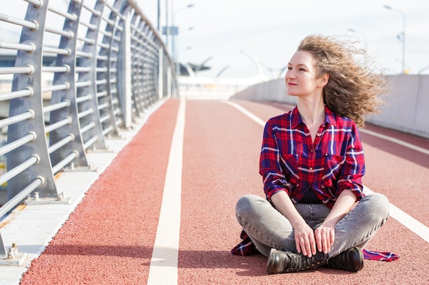 Femme heureuse fatiguée se reposant après avoir couru assis sur un tapis roulant et souriant