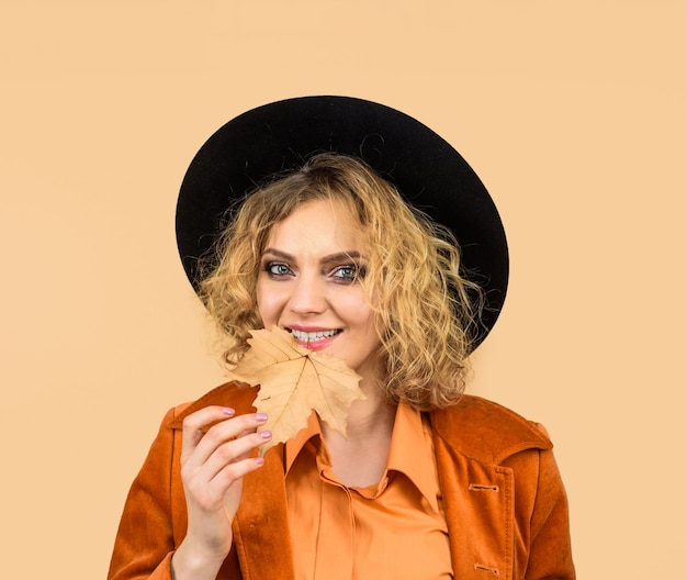 Femme heureuse avec des feuilles d'automne en veste orange fille d'automne au chapeau noir femme à la mode avec