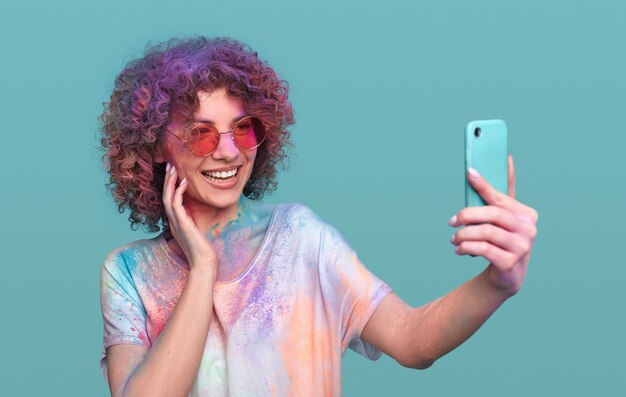 Femme heureuse de hipster avec des couleurs de holi prenant le selfie