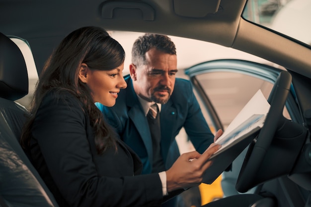 Femme heureuse à l&#39;intérieur de la voiture dans le salon de l&#39;automobile avec le concessionnaire automobile.