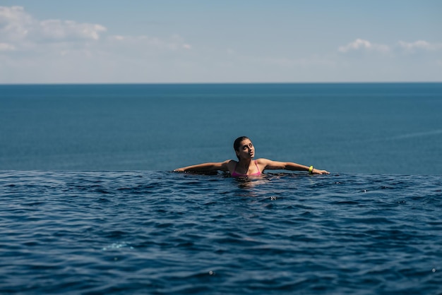 Femme heureuse en maillot de bain nageant dans une piscine à débordement contre le front de mer
