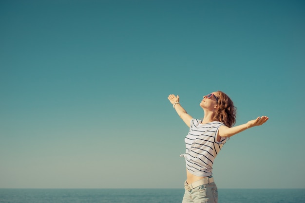 femme heureuse avec les mains ouvertes contre la mer et le ciel bleus